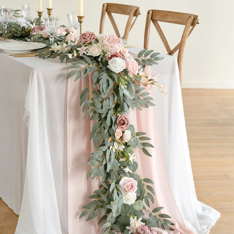 A floral garland featuring pink and white roses and eucalyptus leaves draped across a white tablecloth.