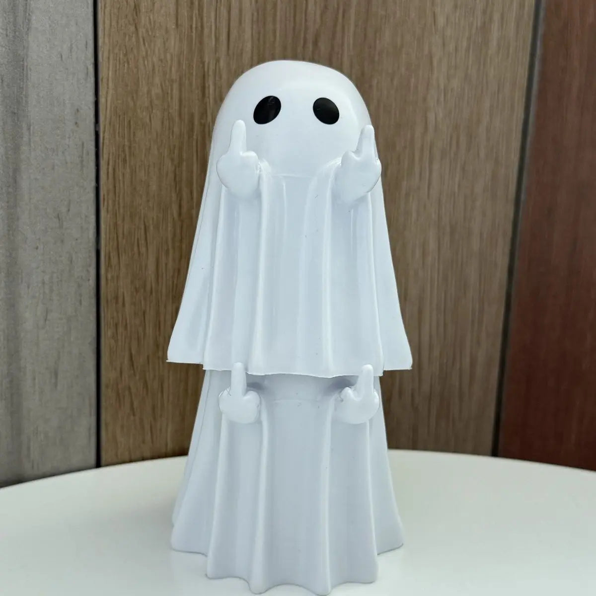 A white ghost figurine with a hood and round eyes standing on a white surface.