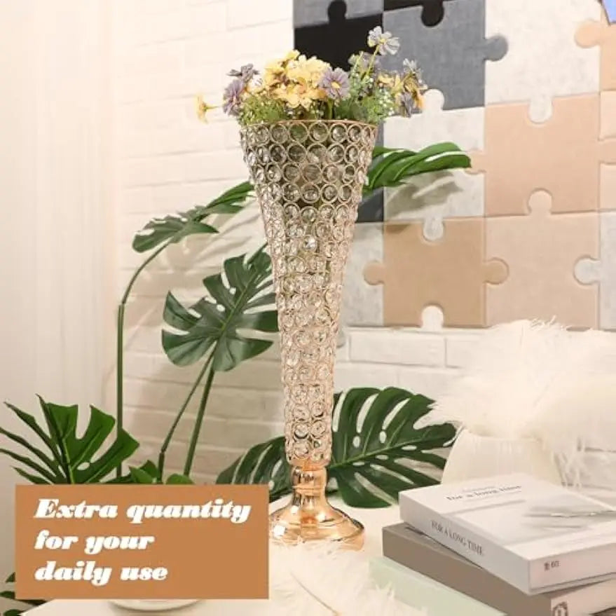 Goldener Kristallvase mit lila und gelben Blumen auf weißer Fläche neben grünen tropischen Blättern.