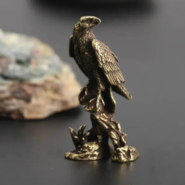 A vintage brass eagle statue miniature desk sculpture standing on a dark surface.