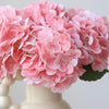 A cluster of pink artificial hydrangea flowers displayed in a white ceramic vase.