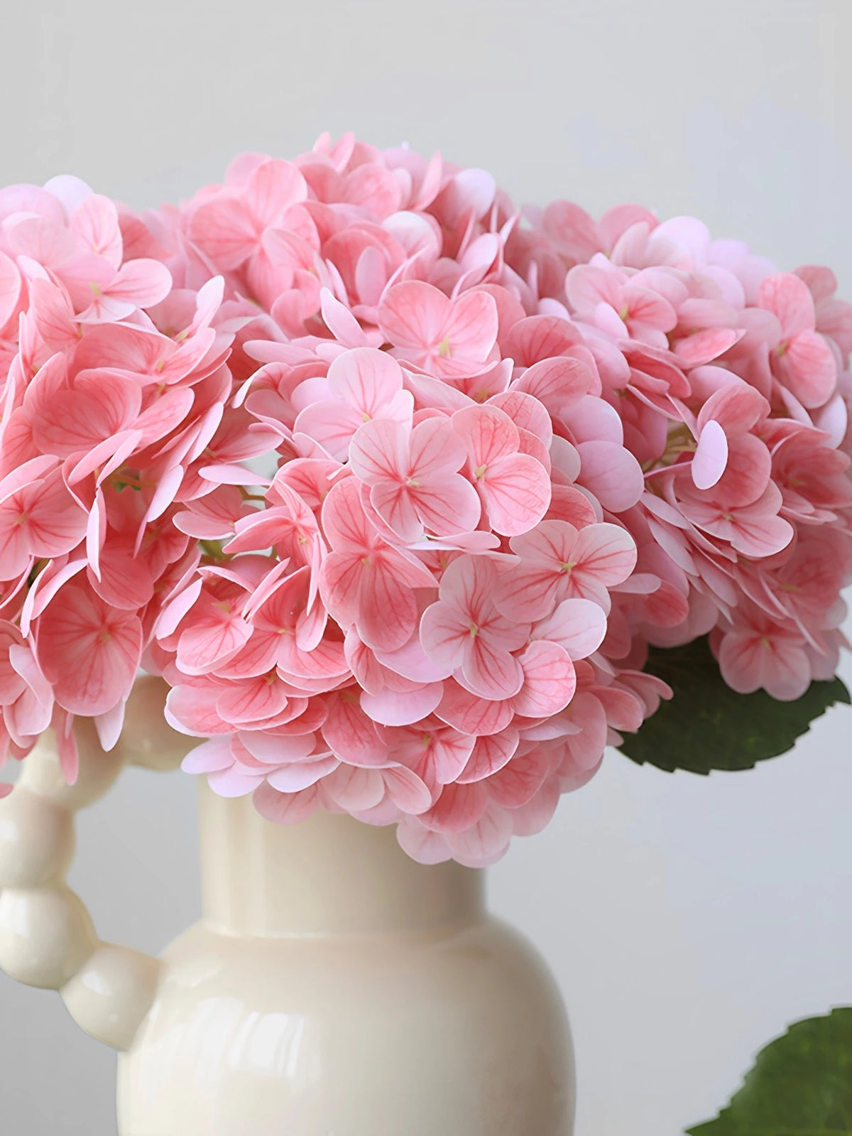 A cluster of pink artificial hydrangea flowers displayed in a white ceramic vase.