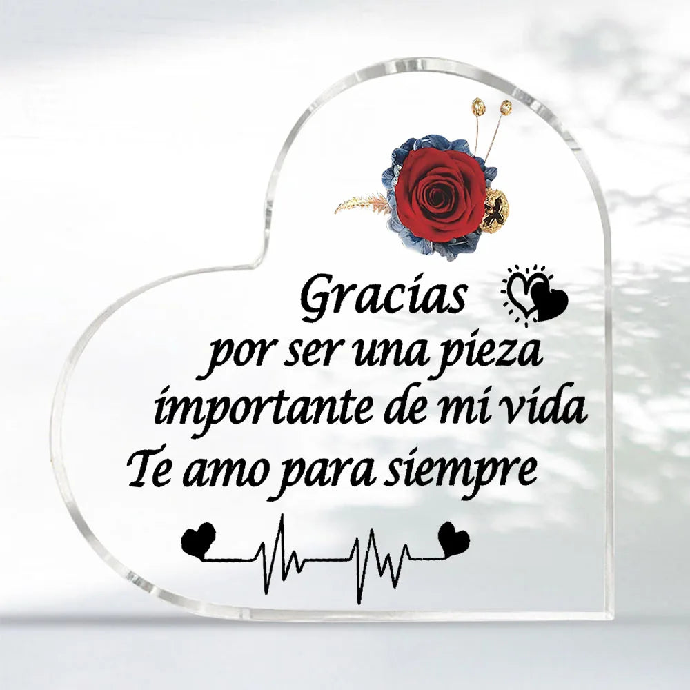 A clear heart-shaped glass keepsake frame with a red rose and text that reads Gracias por ser una pieza importante de mi vida