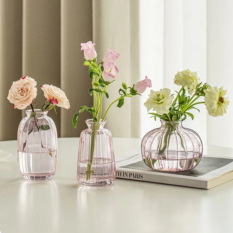 Three glass vases holding pink and white roses on a white table.