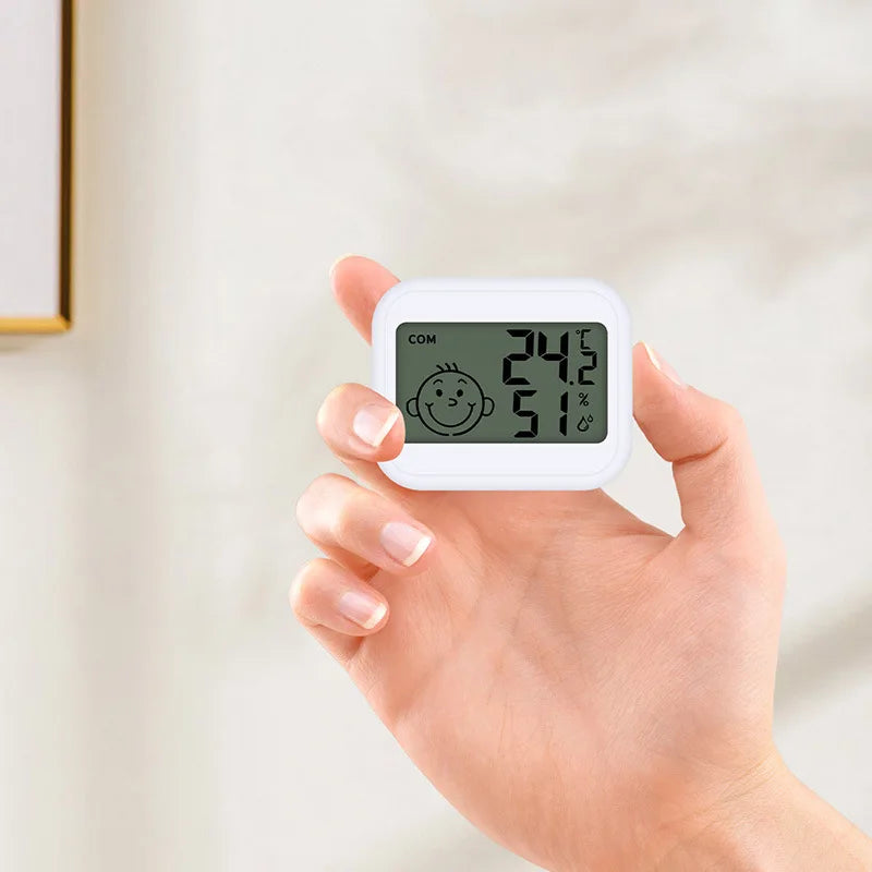 A hand holds a white LED digital thermometer displaying 24.2 degrees Celsius and 51% humidity.