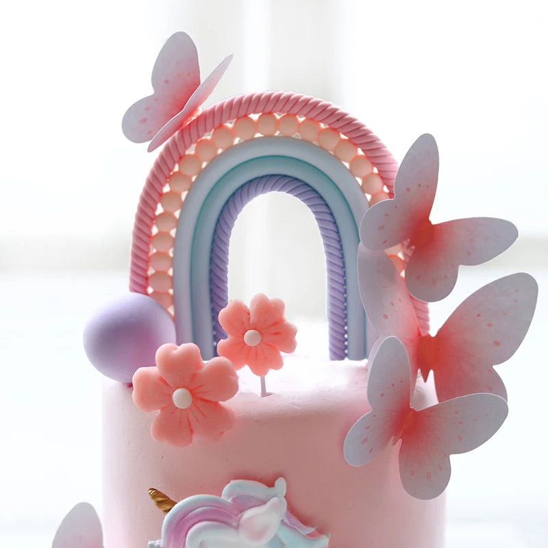 Pink unicorn theme cake topper set featuring a rainbow arch and pink butterflies on a light pink cake.