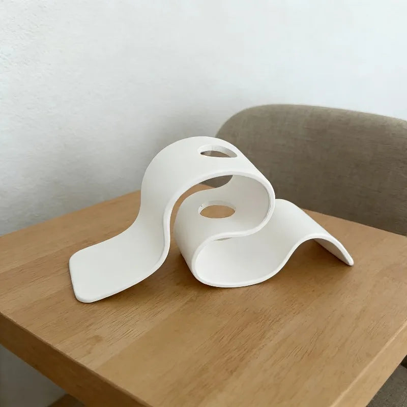 Jarrón decorativo moderno curvo blanco hecho de material impreso en 3D sobre una mesa de madera.