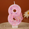 A pink glitter number eight candle decorated with a butterfly on a wooden surface.