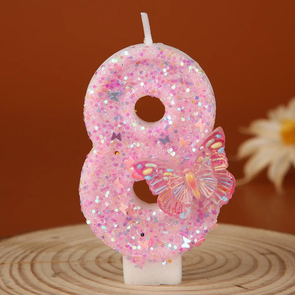 A pink glitter number eight candle decorated with a butterfly on a wooden surface.