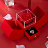 A red velvet box contains a rose and an elegant gold pendant necklace on a red satin background.