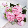 A bouquet of pink silk rose and peony artificial flowers resting on a white surface next to a book.