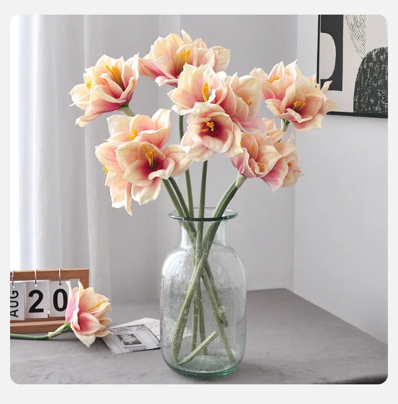 A vase of artificial Clivia Amaryllis flowers in soft peach and cream tones on a gray surface.