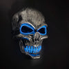 A realistic latex skull mask with glowing blue eyes and teeth against a dark background.