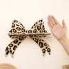A leopard print bow-shaped wall mounted storage rack is displayed against a light background with a hand visible.