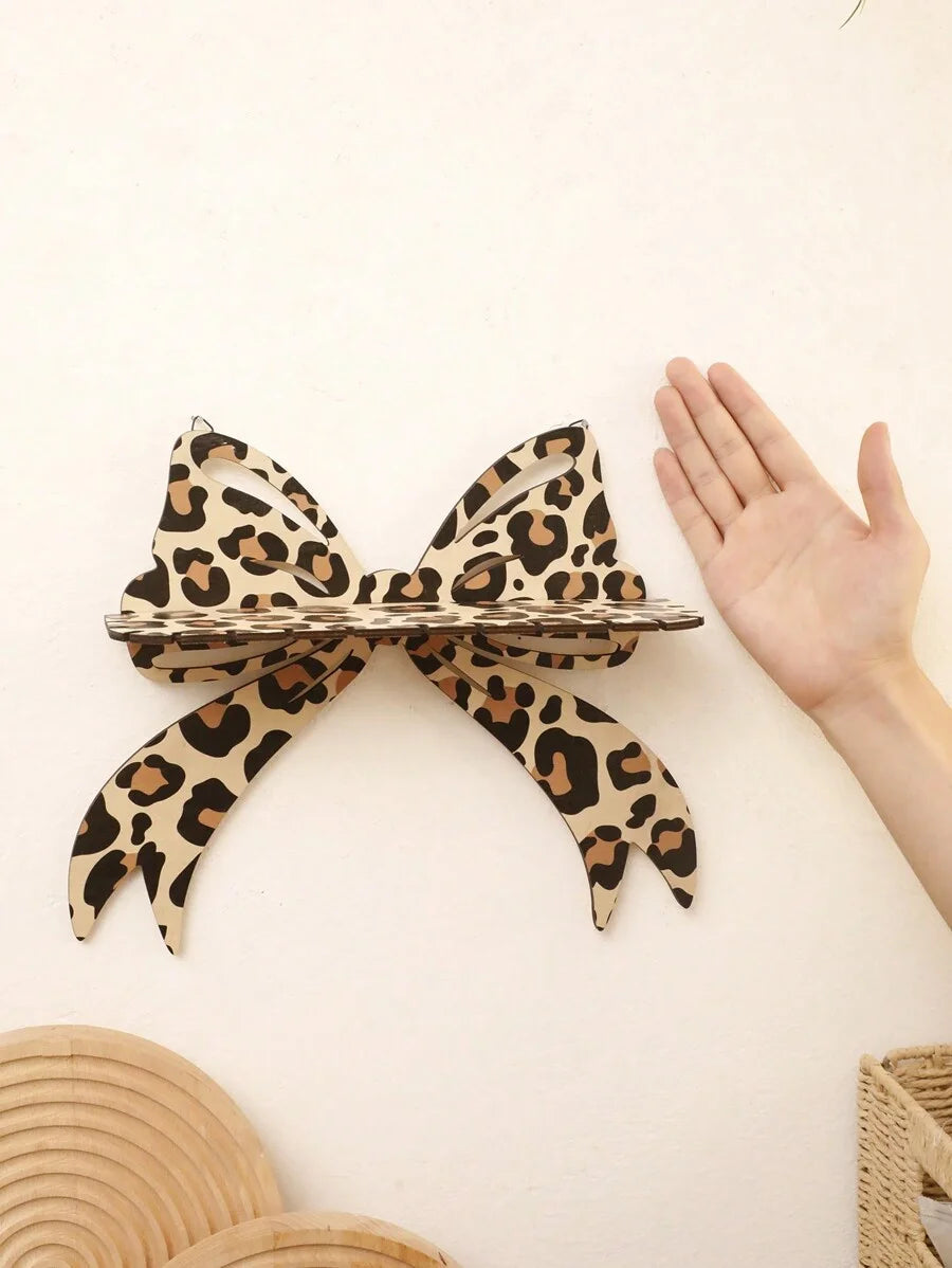 A leopard print bow-shaped wall mounted storage rack is displayed against a light background with a hand visible.