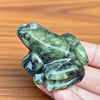 Une figurine de grenouille de jade miniature tenue dans la main d'une personne sur un fond en bois.