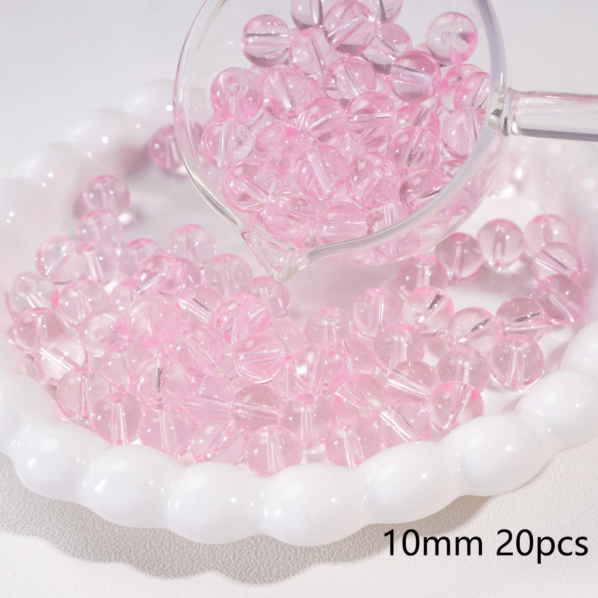 A clear glass magnifying glass shows pink round spacer beads scattered on a white dish.
