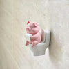 Figurine de cochon en céramique rose assise sur un siège de toilette blanc.