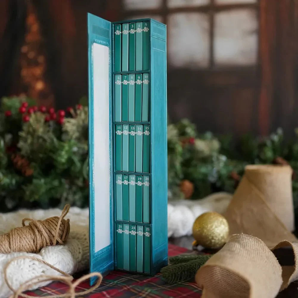 A vertical teal advent calendar box with twelve numbered compartments and decorative ornaments resting on a rustic fabric.