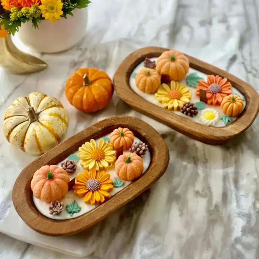 A wooden tray holds orange and yellow pumpkin-shaped candles in a silicone mold kit on a white surface.
