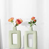 Two light green geometric ceramic vases holding orange and pink roses on a wooden surface.