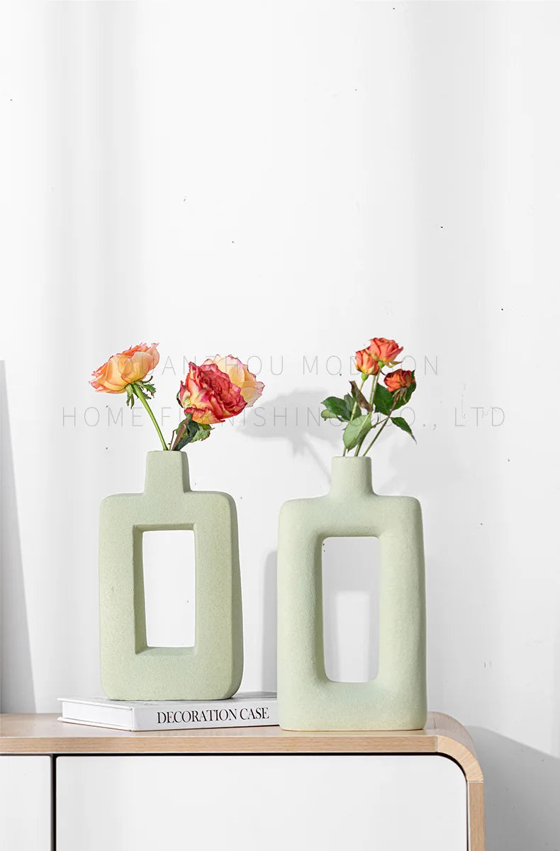 Two light green geometric ceramic vases holding orange and pink roses on a wooden surface.