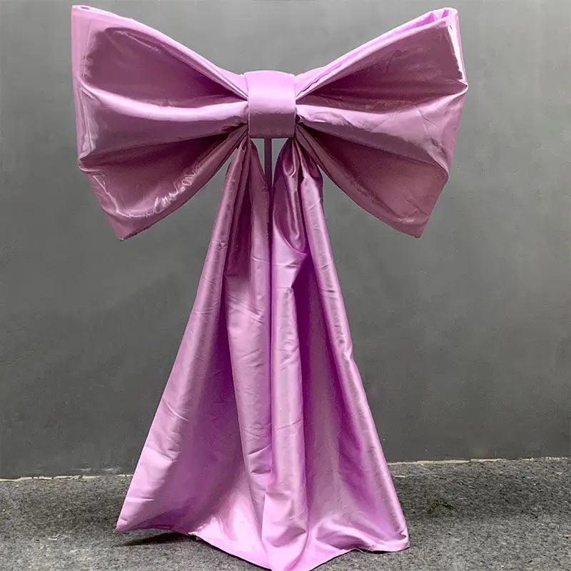 A large lilac satin bow with long tulle drape used for event decoration.