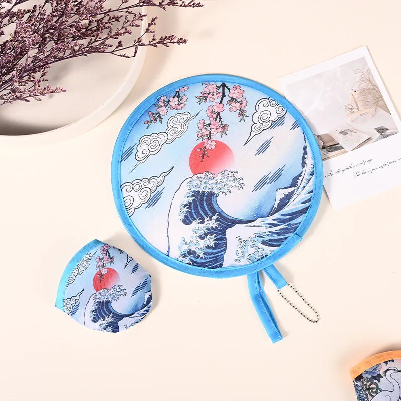 A blue fabric hand fan featuring a Japanese wave design and cherry blossoms, shown with a hanging chain.