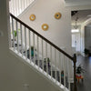 A wooden staircase railing with white spindles and three gold sunflower wall mirrors on a light gray wall.