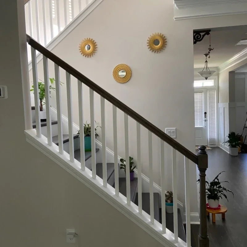 A wooden staircase railing with white spindles and three gold sunflower wall mirrors on a light gray wall.