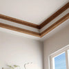 A close-up of crown molding trim in a warm brown color installed on a white ceiling and wall.