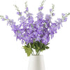 Un bouquet de fleurs artificielles de delphinium violet dans un vase blanc.