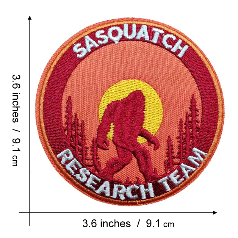 An embroidered patch featuring a red Bigfoot silhouette against a yellow sun, with the text SASQUATCH RESEARCH TEAM.