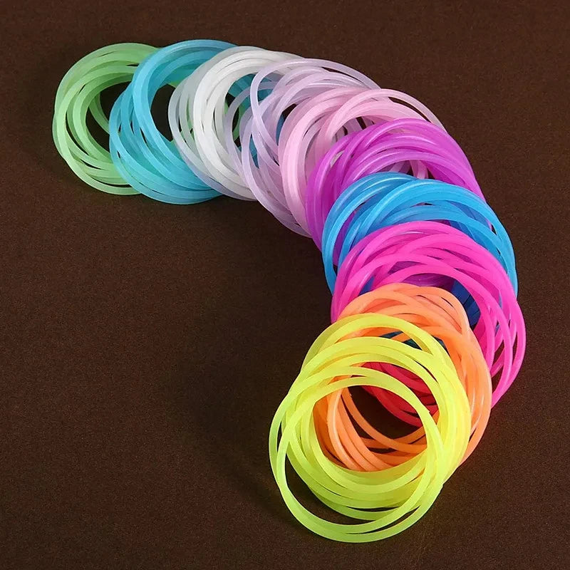 A collection of ten glow-in-the-dark silicone bracelets in a rainbow gradient are arranged in a curved line.