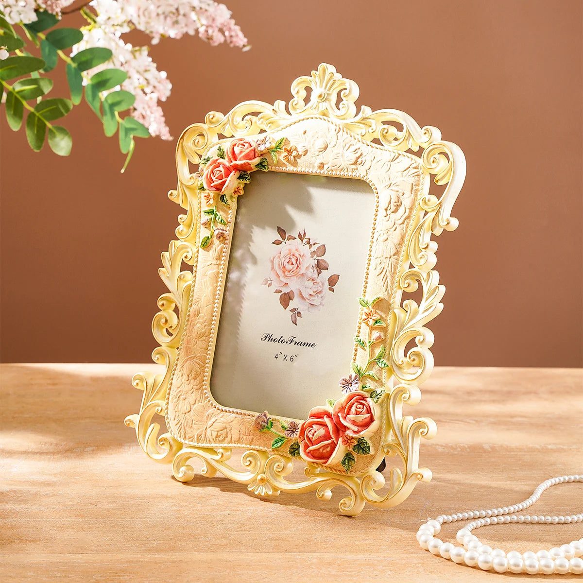 A vintage gold-framed resin photo frame decorated with roses and greenery, resting on a wooden surface.