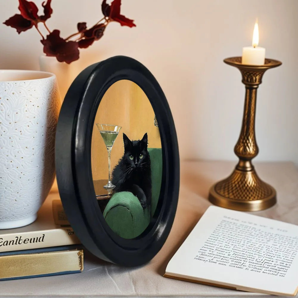 A framed picture of a black cat sitting on a green cushion, displayed next to a gold candle holder and books.
