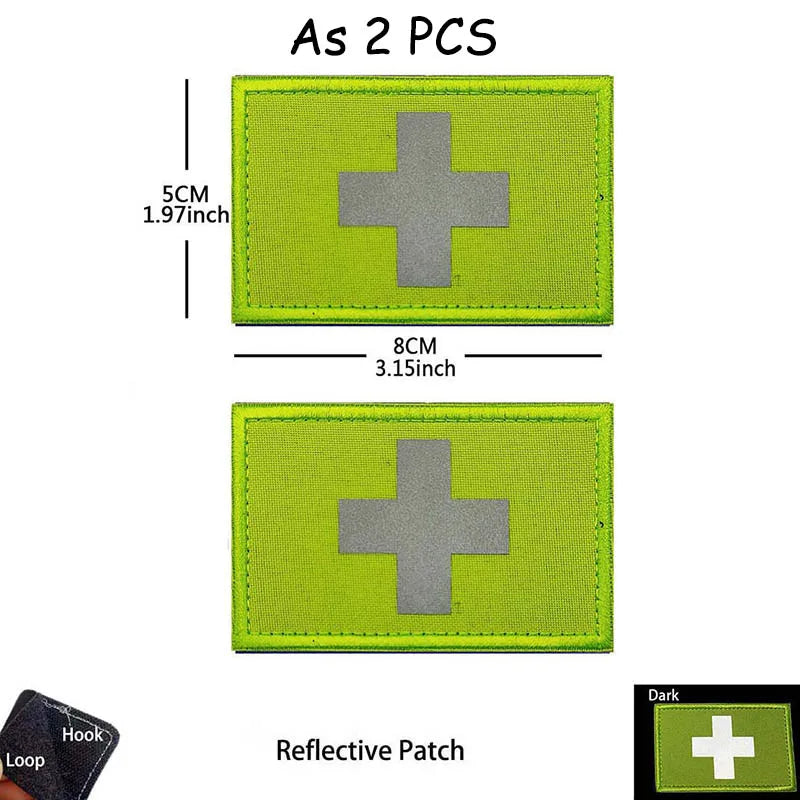 A rectangular olive green reflective patch with a silver cross design, measuring 5cm by 8cm.