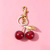 A gold chain charm with a loop and a leaf pendant is displayed against a pink background.