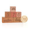 A stack of wooden baby milestone cards showing numbers 5, 7, and 0 with the word easter days on the bottom card.