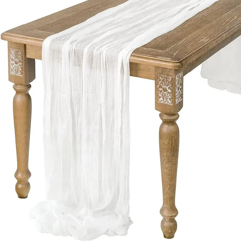 A white gauzy fabric table runner draped over a wooden table.