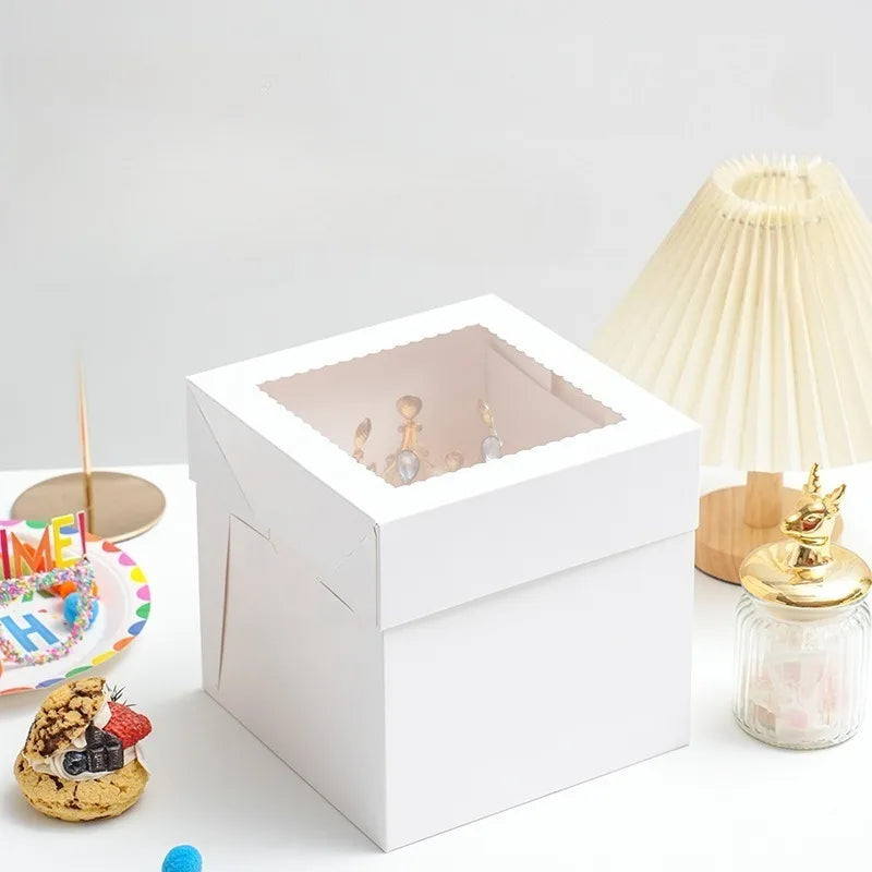 White bakery boxes with a window displaying small pastries and cakes on a white surface.