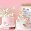 A white cake decorated with pink butterfly toppers and a gold birthday circle on a pink background.