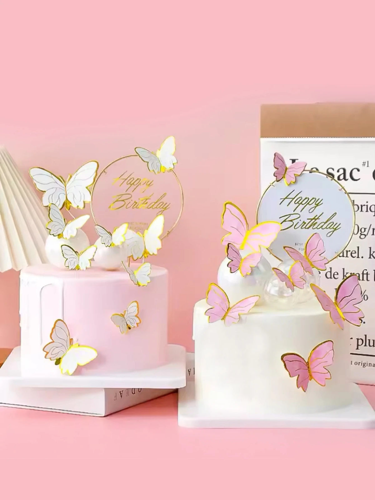 A white cake decorated with pink butterfly toppers and a gold birthday circle on a pink background.