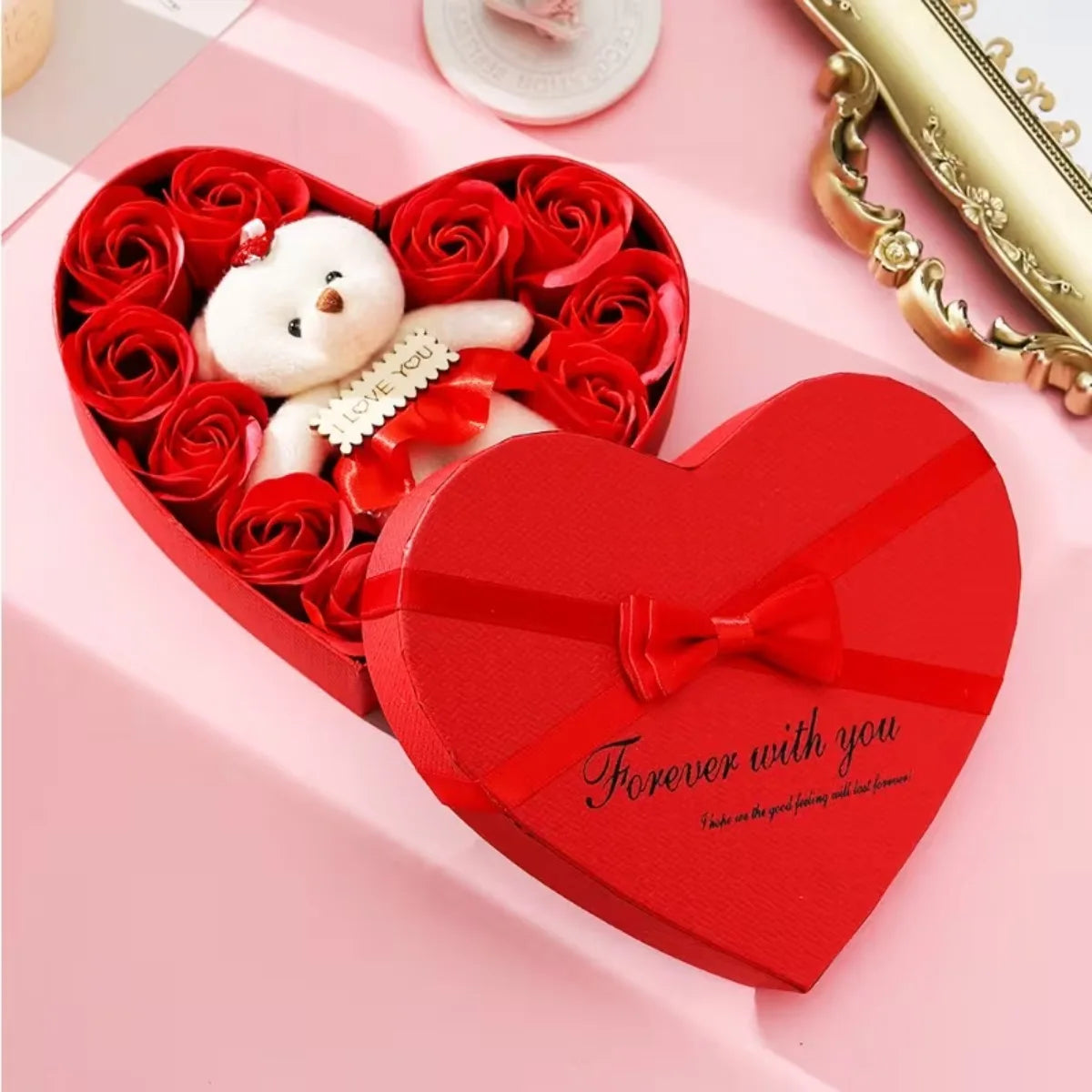 A red heart-shaped gift box filled with red roses and a white plush bear, tied with a red ribbon.