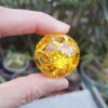 A hand holds a clear, faceted yellow crystal ice crack ball used as water fountain decor.