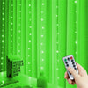A hand holds a smartphone displaying remote control LED curtain fairy lights illuminating bright green curtains.