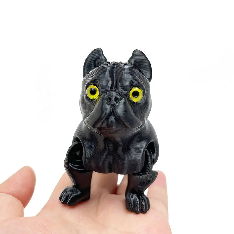 A black 3D printed articulated bulldog figurine with bright yellow eyes is held in a hand.