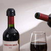 A dark red wine bottle with a black stopper is shown next to a glass of red wine.