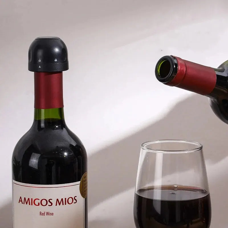 A dark red wine bottle with a black stopper is shown next to a glass of red wine.