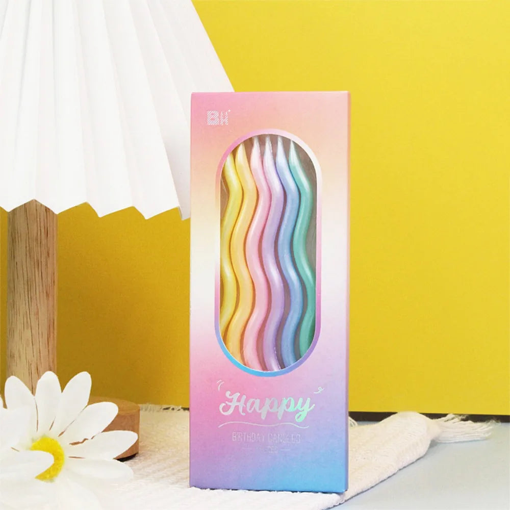 A vertical box of elegant spiral birthday candles in pink and purple hues resting on a white cloth.